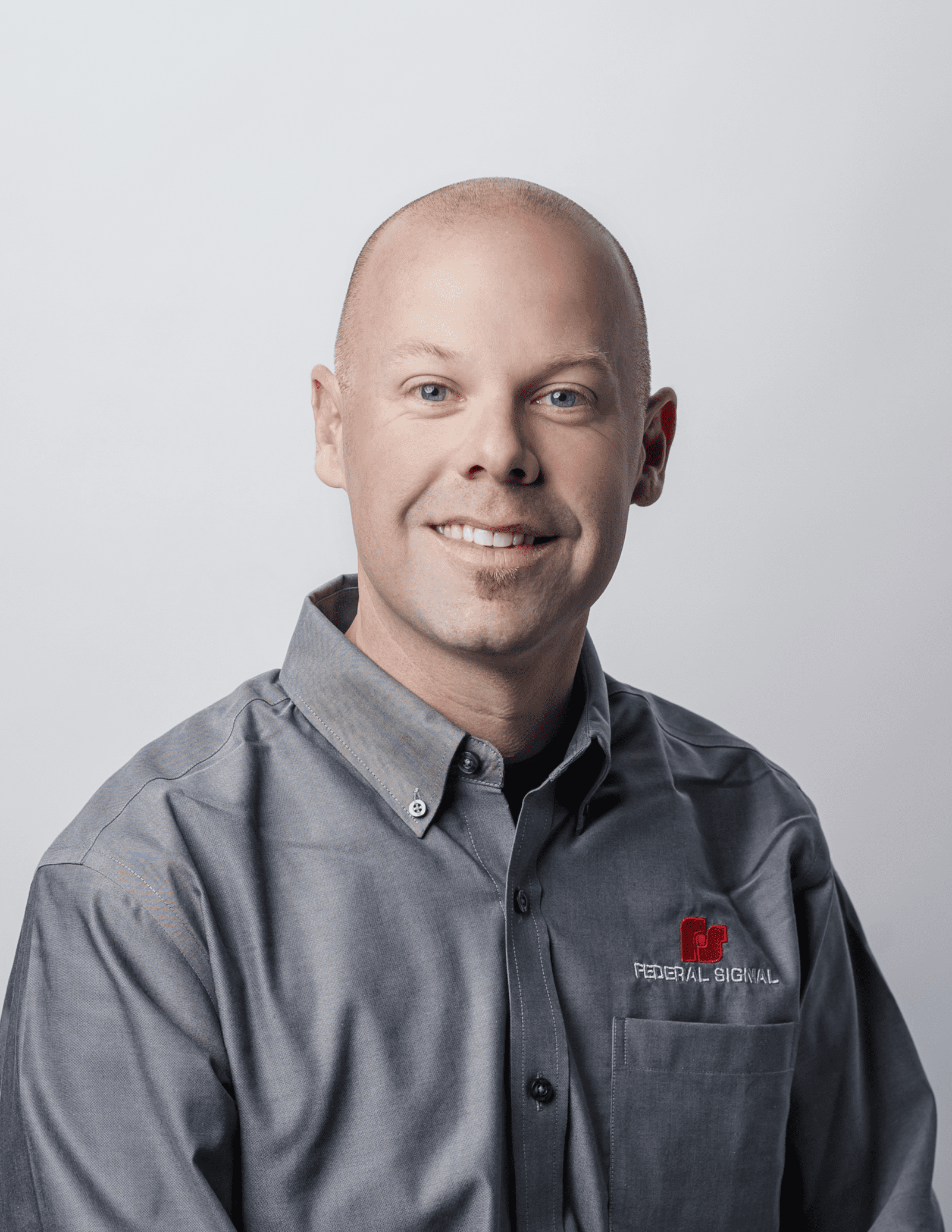A smiling man wearing a gray Federal Signal shirt poses in front of a neutral background.