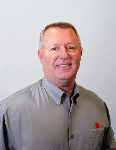 A man in a gray shirt is smiling against a plain background.