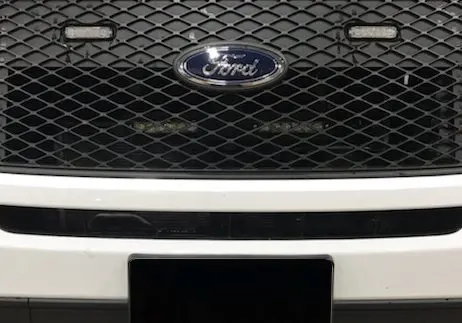 Close-up of a Ford truck grille with a black mesh pattern and the Ford logo at the center.