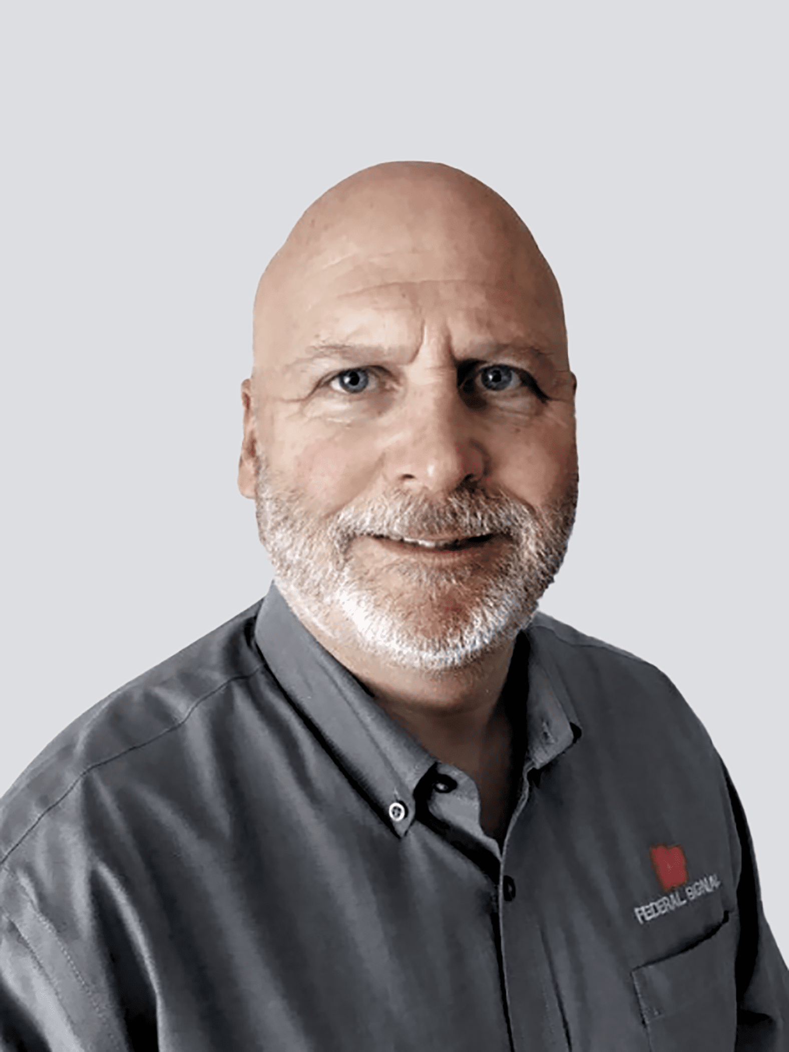 A man with a bald head and beard wearing a gray shirt stands against a plain background, smiling slightly.