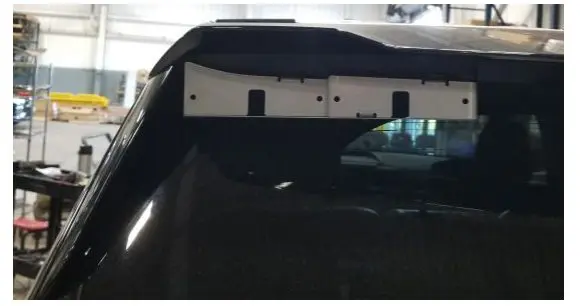 A rear view of a vehicle's roof with a mounted white bracket inside a garage. Shelves and equipment are visible in the background.