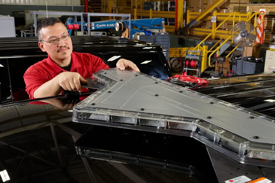 Person in a red shirt assembling or inspecting a large, black and gray electronic device in an industrial setting.
