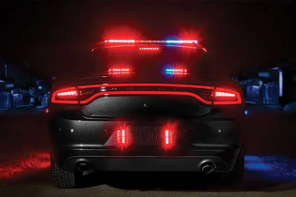 A police car with flashing red and blue lights is shown from the rear at night.