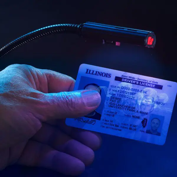 Person holding an illuminated Illinois driver's license under a UV light.