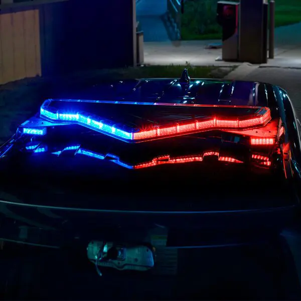 Red and blue police car lights flash in the dark parking area.