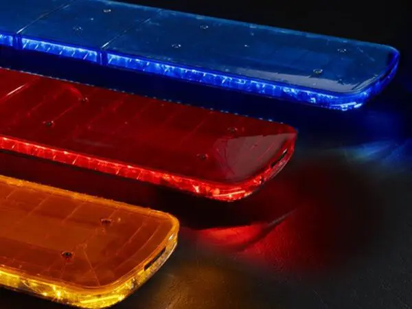 Federal Signal emergency vehicle light bars in blue, red, and yellow are illuminated and placed on a dark surface.