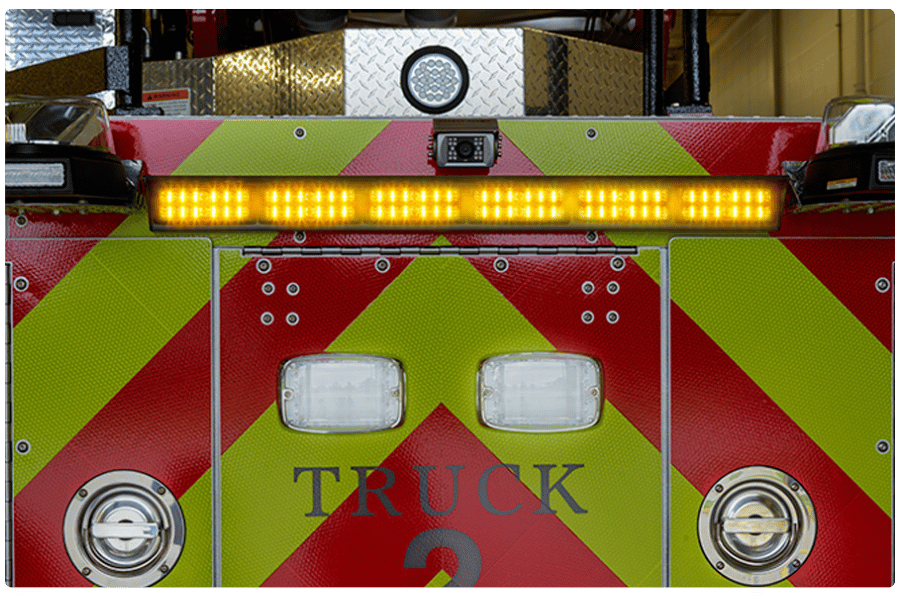 Close-up of a fire truck's front with red and yellow diagonal stripes, illuminated amber lights, and the word "TRUCK" visible.