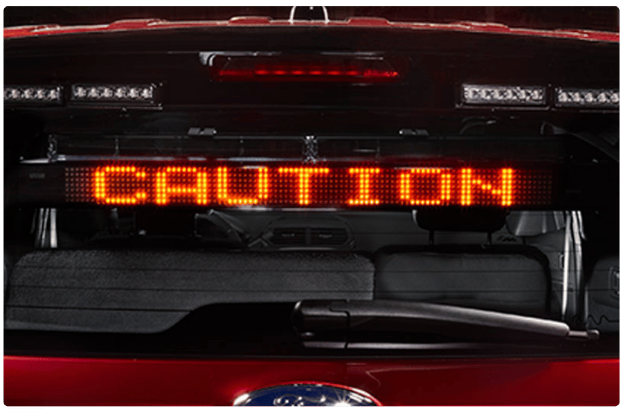 A red LED sign inside a vehicle displays the word "CAUTION" in bright orange letters.