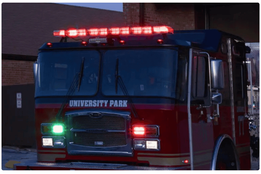 A red fire truck with flashing red and green lights is parked in front of a building. The truck has "University Park" written on the front.