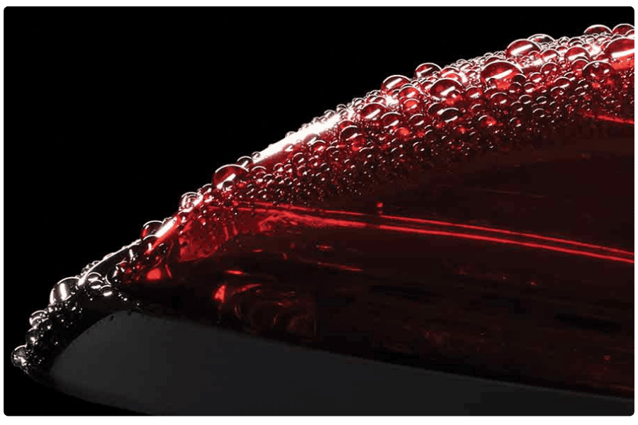 Close-up of a red car tail light covered in water droplets against a black background.