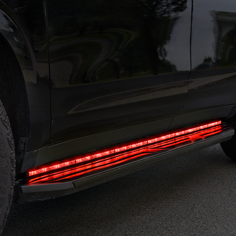 Close-up of a black vehicle parked on a road, featuring an illuminated red LED strip along the lower side panel.