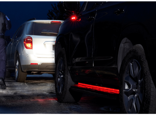 A police officer stands beside two cars stopped on a wet road at night, with the vehicles' brake lights illuminated.