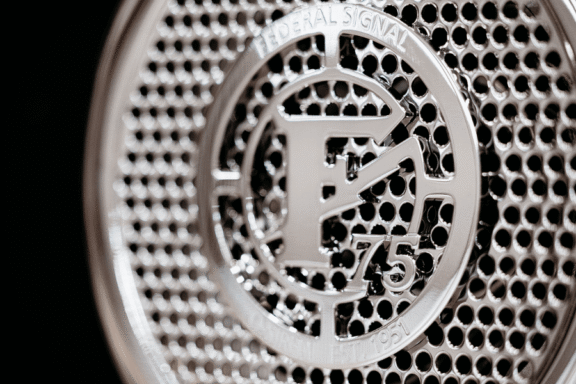Close-up of a metallic Federal Signal speaker grille with the letter "F" and the number "75" embossed in the center.