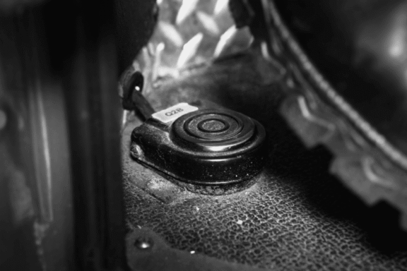 Close-up of a black foot pedal switch labeled "STOP" on a textured floor next to a vehicle tire.