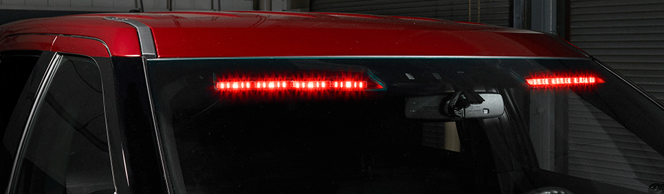 Rear view of a red vehicle showing a high-mounted LED brake light in action inside a dimly lit garage.