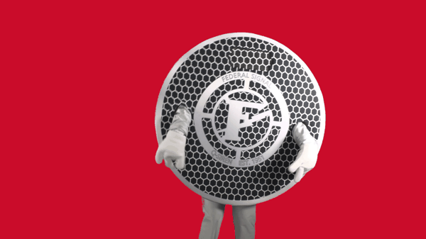 Person in a large, round costume resembling a Federal Signal manhole cover stands against a solid red background.