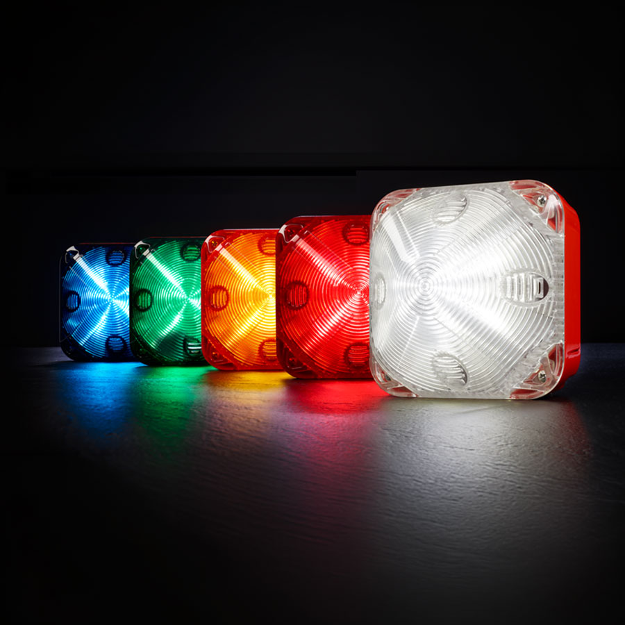 Five square signal lights in blue, green, yellow, red, and white are lined up on a dark surface, illuminated from within.