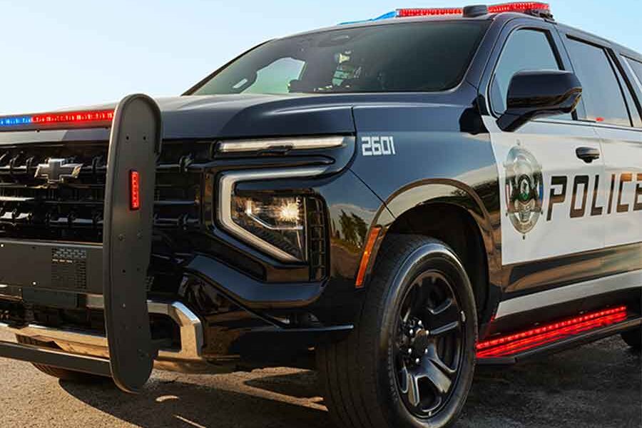 A black police SUV equipped with the DynaFlare® Emergency Vehicle Perimeter Light, displaying red and blue lights, is parked on a paved surface. The vehicle features POLICE markings and a push bumper on the front.